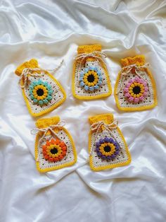 four small crocheted bags with colorful flowers on them sitting on a white sheet