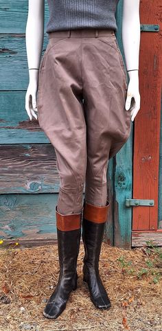 a mannequin wearing brown pants and boots in front of a wooden wall with blue shutters