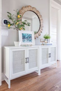 a white sideboard with two doors and a mirror above it on the wall next to a potted plant