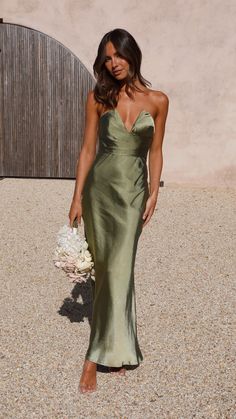 a woman in a long green dress holding a white bouquet and posing for the camera