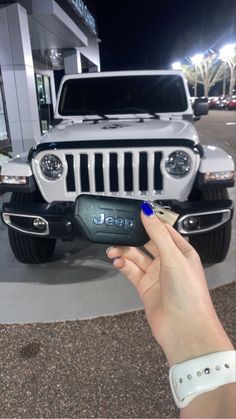 a hand holding a remote control in front of a white jeep