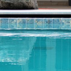 an empty swimming pool with rocks in the back ground and water reflecting on the surface