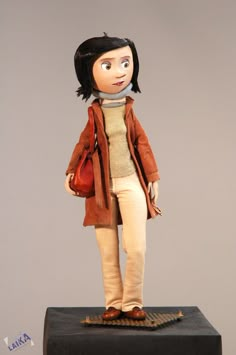 a doll is standing on top of a black box with a red purse in it's hand