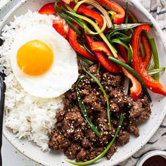 a white plate topped with rice and meat next to an egg on top of it