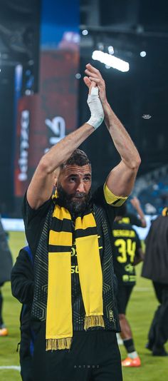 a man in black and yellow scarf holding his hands up