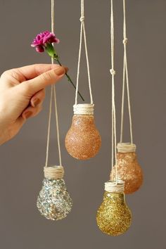 three hanging lights with flowers in them and one being held by a person's hand