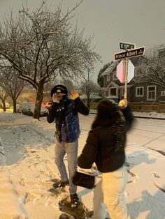 two people standing in the snow next to a street sign