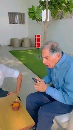 an older man sitting on a chair looking at his cell phone while another person sits next to him