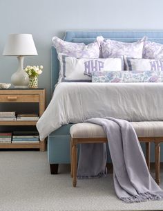 a bed with pillows and blankets on top of it next to a night stand filled with books