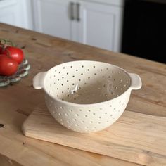 a white colander sitting on top of a wooden table next to tomatoes and a bowl