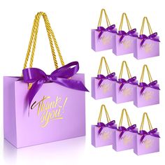 purple gift bags with gold foil lettering and a purple ribbon tied around the handles that say thank you