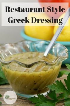 a glass bowl filled with greek dressing next to lemons and parsley