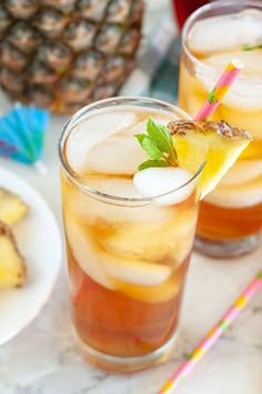 two glasses filled with iced tea on top of a table next to pineapples