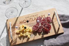 a wooden cutting board topped with meat and cheese next to wine glasses on a table