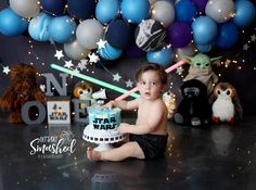 a baby boy sitting in front of a star wars cake