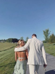 a man and woman walking down a path in the grass with their back to each other