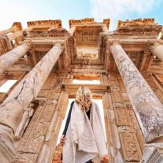 a woman standing in front of an ancient building with columns and pillars on either side