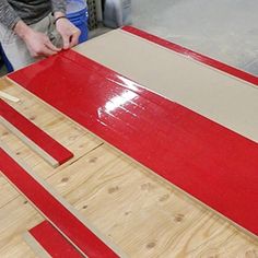 a man is working on some red and white wood planks that are being made