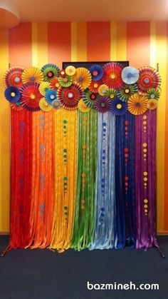 a rainbow colored backdrop with flowers and ribbons on the wall in front of it is an orange striped wall