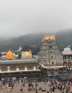 many people are walking around in front of a temple on a foggy day with mountains in the background