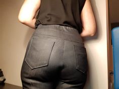 a woman standing in front of a wall with her back to the camera and wearing black pants