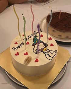 a birthday cake with lit candles on it sitting on a table next to another cake