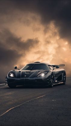 a black sports car driving down a road under a cloudy sky with dark clouds in the background