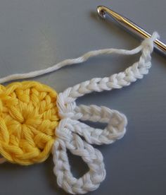 a crocheted yellow and white object on top of a gray table next to a knitting needle