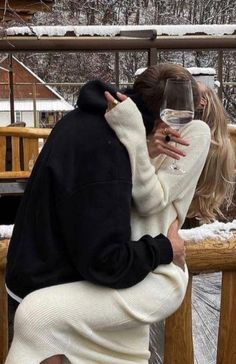 a man and woman kissing with a glass of wine in front of snow covered trees