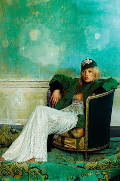 a woman sitting in a chair wearing a green jacket and white dress with her legs crossed