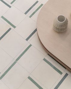 a vase sitting on top of a wooden table next to a white and green tile floor