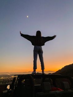 a woman standing on top of a truck with her arms outstretched in front of the sun