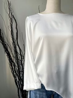 Introducing our stunning White Long Blouse, crafted with utmost elegance and made from luxuriously soft satin material. This versatile wardrobe essential is designed to effortlessly elevate your style and provide unmatched comfort throughout the day. The front of this exquisite blouse features a gracefully curved cut that starts at the waist and cascades down to the bottom, adding a touch of sophistication to your ensemble. The unique curve emphasizes your natural waistline, creating a flattering silhouette that complements all body types. Indulge in the unparalleled softness of the satin material that glides against your skin, offering a gentle and sensual embrace throughout the day. The silky texture not only feels incredibly soft but also adds a touch of glamour to your outfit, making t Classic White Satin Blouse, Sleek Solid Silk Blouse, Long Sleeve Satin Finish Top For Formal Occasions, Formal Long Sleeve Top With Satin Finish, White Satin Tops For Workwear, Long Sleeve Tops With Satin Finish For Formal Occasions, Elegant Formal Plain Tops, Elegant White Plain Blouse, Elegant Plain Tops For Formal Occasions