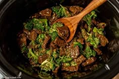 beef and broccoli in a crock pot with a wooden spoon on top