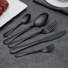 six spoons, one fork and two knives on a table next to a plate with steak