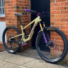 a yellow and purple mountain bike parked in front of a brick building next to a door