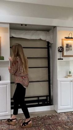 a woman walking through a living room with white walls and shelving unit behind her