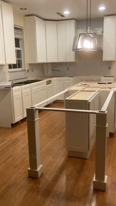 an empty kitchen with wooden floors and white cabinets in the middle, is seen from across the room