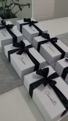 six white boxes with black ribbons tied around the top and bottom, sitting on a table in front of a potted plant