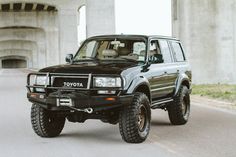 a black four - doored toyota truck driving down the road in front of an overpass