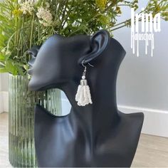 a black mannequin head with white earrings on it and flowers in the background