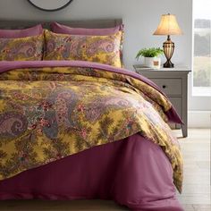 a bed with a yellow and purple comforter on top of it next to a night stand