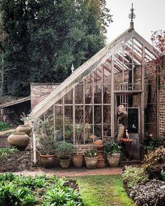 a woman standing in a greenhouse with potted plants and pots on the ground next to it