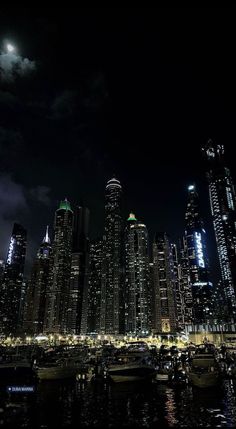 the city skyline is lit up at night with boats in the water and lights on