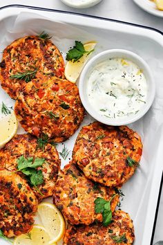 crab cakes with lemons and herbs on a white platter next to dipping sauce