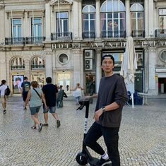 a man standing on top of a scooter in front of a large building