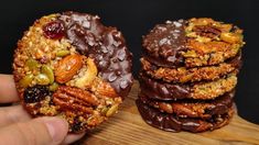 a person holding a chocolate covered cookie with nuts and raisins on it next to other cookies