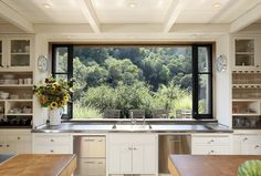 a kitchen with an open window overlooking the trees and bushes in the distance is shown