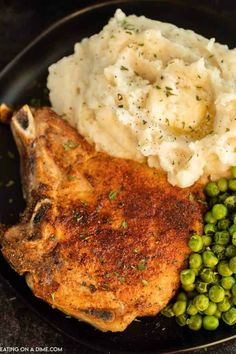 a black plate topped with chicken, mashed potatoes and peas