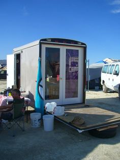 a man sitting in a chair next to a small trailer with a door on it